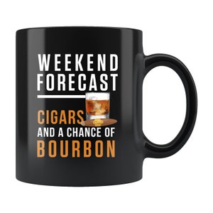 以下が含まれることがあります： 白い文字で「週末予報：シガーとバーボンを味わうチャンス」と書かれた黒いコーヒーカップ。カップには、琥珀色の液体が入ったグラスとシガーのグラフィックが描かれている。