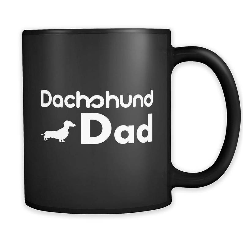 May include: Black coffee mug with white text that reads "Dachshund Dad" and a white silhouette of a dachshund.