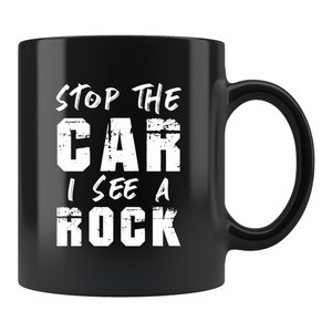 Könnte beinhalten: Schwarze Keramik-Kaffeetasse mit weißem Text, der "Stop the car I see a rock" lautet.
