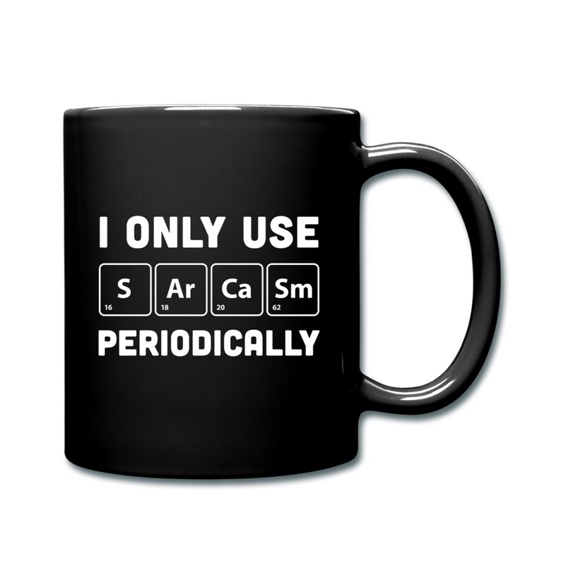 Op de afbeelding: Zwarte koffiemok met witte tekst die "I only use S Ar Ca Sm periodically" luidt. De letters staan in vakjes met de atoomnummers eronder.