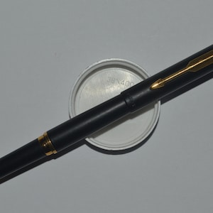 May include: A black and gold pen with a gold clip and a black barrel. The pen is lying on a white surface.