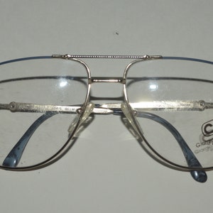 Könnte beinhalten: Goldfarbene Aviator-Brille mit blauen Bügeln und klaren Gläsern. Die Brille trägt das Giorgio Armani Logo am rechten Bügel.