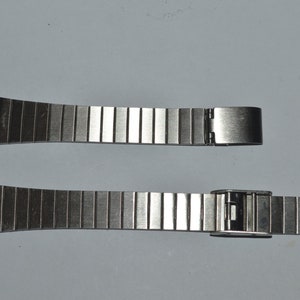 May include: Two silver watch bands with a clasp on one end. The bands are made of metal links.