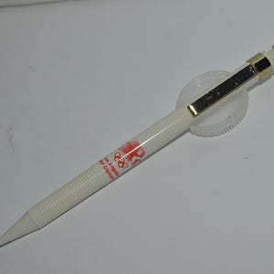 May include: White mechanical pencil with a gold-colored clip and a red and white printed design that says "Los Angeles 1984 Olympic Games".