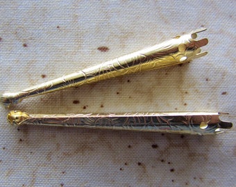 May include: Two gold-colored metal crochet hooks with intricate floral designs. The hooks have a pointed end and a decorative top.