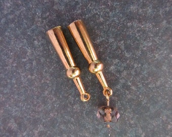 May include: Two gold-colored metal earring components with a cylindrical top and a small ball in the middle. Each component has a small loop at the bottom. A faceted, smoky-colored bead hangs from one of the components.