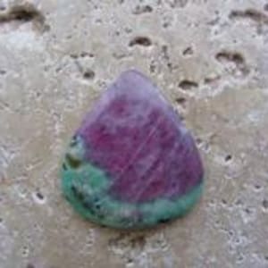 May include: A teardrop-shaped cabochon gemstone featuring a vibrant magenta-pink center surrounded by a mottled light green border with dark speckles throughout the surface, displaying a smooth, polished finish and natural mineral variations.