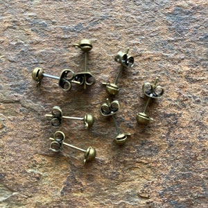May include: A close-up of eight gold-toned earring backs. The backs are made of metal and have a small loop on the back for attaching to an earring.