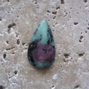 May include: A teardrop-shaped cabochon gemstone featuring a smooth, polished surface with a mottled mix of light green, dark black, and a prominent deep magenta-colored inclusion centered within the stone's body.