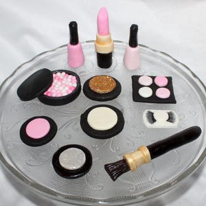 May include: A set of miniature cake decorations featuring makeup items, including a lipstick, nail polish, eyeshadow palettes, blush, and a makeup brush. The decorations are made of fondant and are perfect for a cake themed around beauty and makeup.