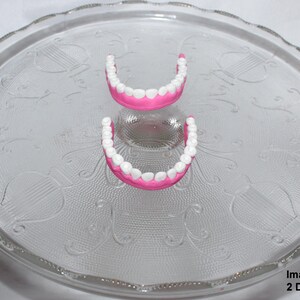 May include: Two sets of pink and white dentures on a clear glass plate with a decorative pattern.
