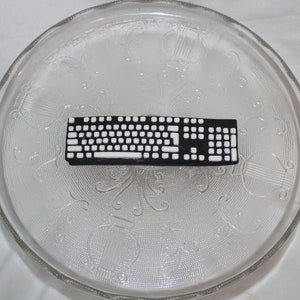May include: A black and white keyboard cake decoration on a clear glass plate with a decorative pattern.