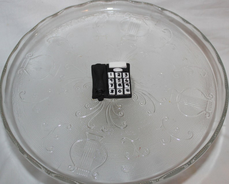 May include: A black and white toy telephone with a rotary dial and number buttons. The toy is on a clear glass plate.