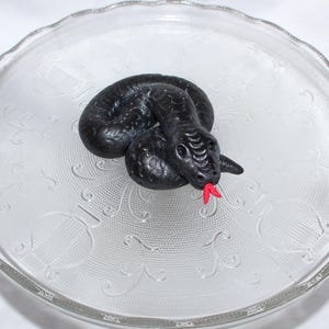May include: A black snake-shaped candy on a white plate with a decorative pattern.