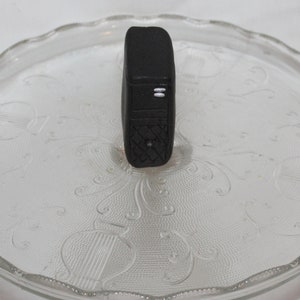 May include: A black fitness tracker with a textured surface and two white lines on the front.