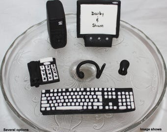 May include: A black computer monitor with the text "Darby & Shane" on the screen, a black computer tower, a black keyboard, a black telephone, a black headset, and a black mouse. The items are arranged on a clear glass surface.