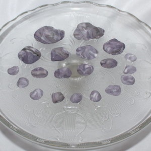 May include: A collection of 15 purple and white agate stones on a white glass plate.
