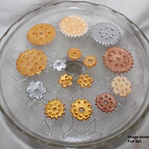 May include: A set of 13 decorative gear-shaped cake toppers in gold, silver, and brown. The image shows the full set of toppers.
