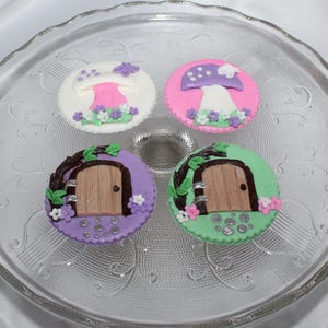 May include: Four decorated sugar cookies on a clear glass plate. Two cookies feature a purple and white mushroom with green leaves and white flowers. The other two cookies feature a brown door with green leaves and pink and white flowers.
