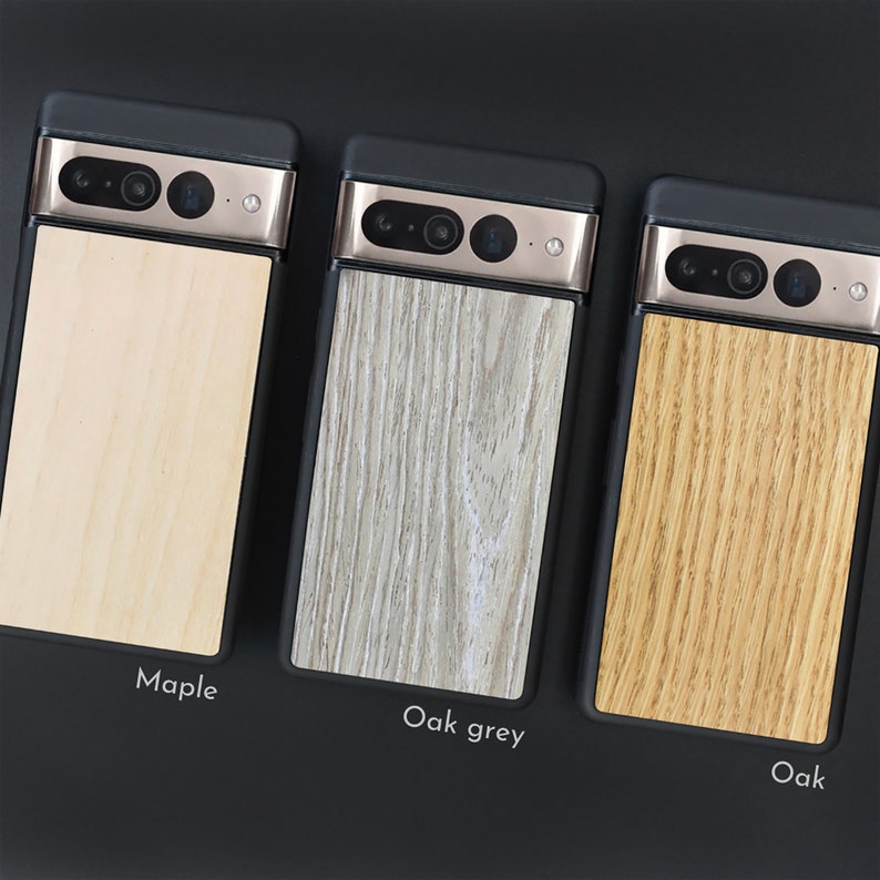 May include: Three phone cases with wooden backings are displayed. The cases have a black frame and a metallic camera bar. The wooden backings are labeled "Maple", "Oak grey", and "Oak", showcasing variations in wood grain and color.