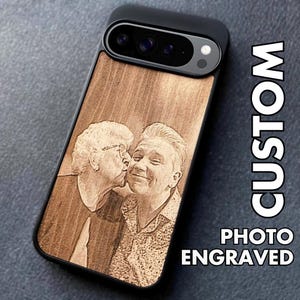 May include: A black phone case with a wooden back, engraved with a photograph of two people kissing. The words "CUSTOM PHOTO ENGRAVED" are printed vertically on the right side.