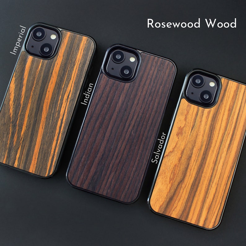 May include: Three iPhone cases with Rosewood Wood designs. The cases feature black borders and varying wood grain patterns, including Imperial, Indian, and Salvador styles. The cases are displayed on a dark surface.