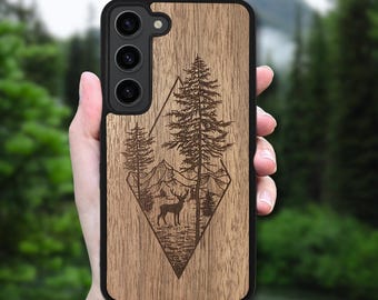 May include: A wooden phone case with a black border. The case features a laser-etched design of a forest scene with mountains, trees, and a deer. The case is designed for a smartphone with three camera lenses.