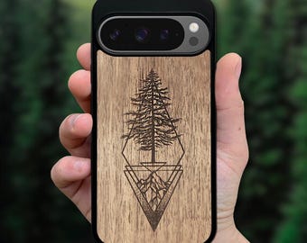 May include: A black smartphone case with a light brown wood grain back panel featuring a laser-engraved black illustration of a tall pine tree positioned above a mountain range, both enclosed within a geometric diamond and triangle frame design.