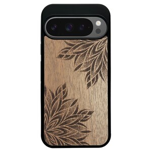May include: A black and wood-toned phone case with a floral design. The case has a black top and sides, with a light brown wooden back. Dark brown floral patterns are etched into the wood, creating a decorative accent.