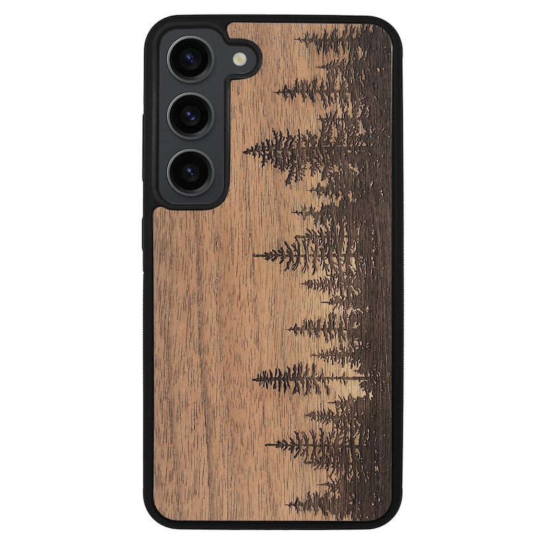 Puede incluir: Una funda de smartphone negra con un panel trasero de madera natural y una escena de bosque grabada con l&aacute;ser. El dise&ntilde;o muestra varios pinos de distintas alturas dispuestos en un patr&oacute;n vertical sobre la textura de madera marr&oacute;n clara.