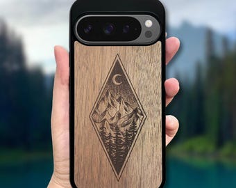 May include: A black smartphone case featuring a wood grain back panel with a laser-engraved diamond-shaped design. The engraving depicts a mountain range, a forest of pine trees, and a crescent moon centered within the diamond frame.