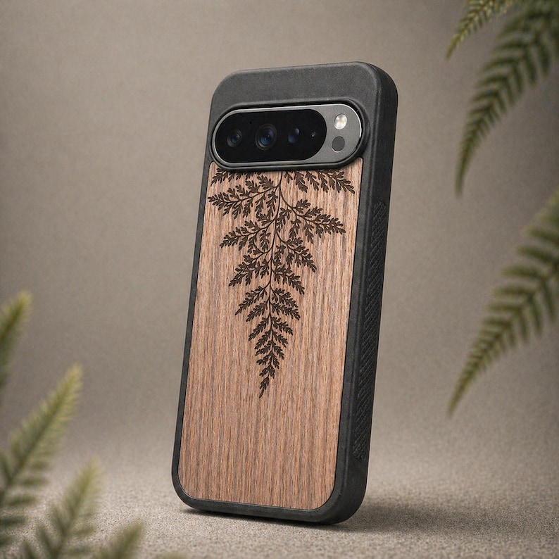 May include: A smartphone case with a wooden panel featuring a fern design. The case has a black border and camera housing. The wood grain is visible, and the fern is etched in a dark brown color. The case is designed to protect the phone.