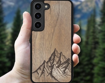 May include: A wooden phone case with a black border. The case features a mountain range design etched into the wood. The phone case is light brown and has three camera lenses.