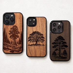 Puede incluir: Tres fundas de teléfono de madera con bordes negros. Cada funda presenta un diseño de árbol diferente grabado en la madera. Los diseños incluyen una escena de bosque, un gran roble y un pino con árboles más pequeños.