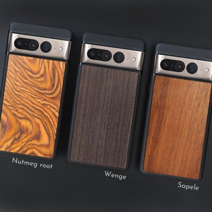 May include: Three phone cases with wooden backings are displayed. The cases have a black frame and a silver camera bar. The wooden backings are labeled "Nutmeg root", "Wenge", and "Sapele", each with a unique wood grain pattern and color.