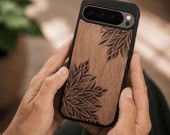 May include: A black smartphone case featuring a natural wood grain back panel with two dark, intricate, dot-work floral mandala patterns etched into the corners. The case has a black frame and a horizontal camera cutout at the top.