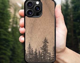 May include: A phone case with a wooden texture and a black border. The case features a forest silhouette design at the bottom. The phone case is held in a hand against a blurred green background.