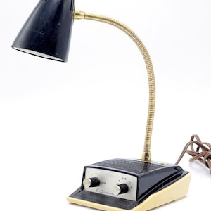 May include: A black and cream vintage 6 transistor radio with a black lamp with a flexible arm. The radio has a volume knob and a tuning knob. The lamp has a black shade.