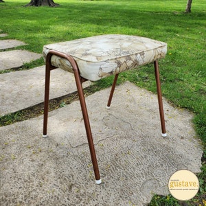 May include: A brown metal stool with white plastic feet. The seat is upholstered in a cream fabric with a floral pattern.