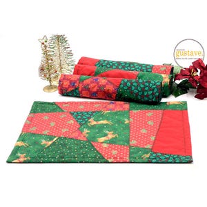 Peut inclure: Un chemin de table de Noël rouge et vert avec un motif patchwork représentant des rennes et du houx. Le chemin de table est en tissu et a une texture matelassée. Le texte "MADE IN gustave.  BROCANTE.ART.DESIGN" est visible dans le coin supérieur droit de l'image.