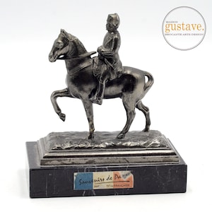 May include: A silver-toned metal statue of a rider on horseback, mounted on a rectangular black marble base. The statue depicts a figure in a military-style uniform. The base has a small label that reads "Souvenirs de Paris".