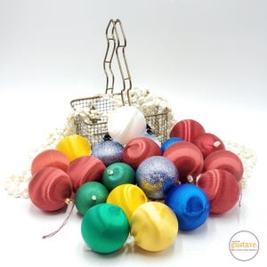 May include: A collection of vintage Christmas ornaments in a variety of colors, including red, green, blue, yellow, and white. The ornaments are made of satin and have a shiny finish. They are arranged in a wire basket with a white string of beads.