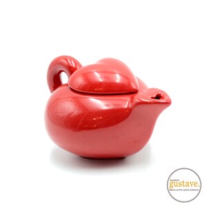 May include: Red ceramic teapot shaped like a heart with a heart-shaped lid. The teapot has a spout and a handle.