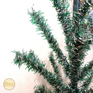 May include: A close-up of a green and silver tinsel Christmas tree. The tinsel is twisted and curled to create a festive look.