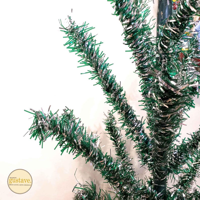 May include: A close-up of a green and silver tinsel Christmas tree. The tinsel is twisted and curled to create a festive look.