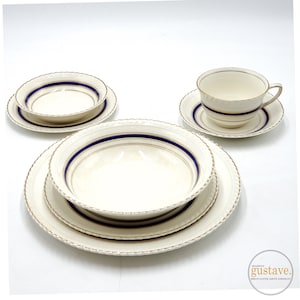 May include: A set of white ceramic dishes with blue and gold trim. The set includes a large bowl, a smaller bowl, a plate, and a teacup and saucer.