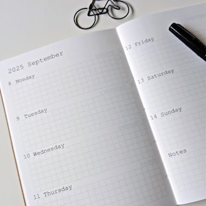 May include: A white gridded notebook with a black pen and a bicycle-shaped paperclip. The notebook has the dates 8-14 and the days of the week Monday through Sunday written on it. The notebook also has the word "Notes" written on it.