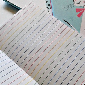 May include: A white notebook with lined pages. The lines are in different colours, including red, yellow, green, and blue.