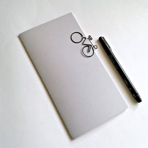 May include: A gray notebook with a black wire bicycle bookmark and a black pen with the word "TOUCH" printed on the side.