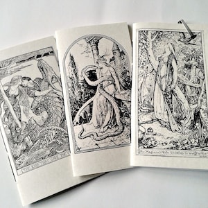 May include: Three off-white paper booklets featuring black ink illustrations. The left booklet shows a couple with a dragon, the centre shows a figure with a snake, and the right shows a person in a forest with the text The Magician's Wife Thistles to the Parrot.